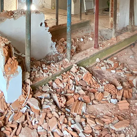 Baustelle im Innenraum mit freigelegtem Mauerwerk, Bauschutt und Stützen.