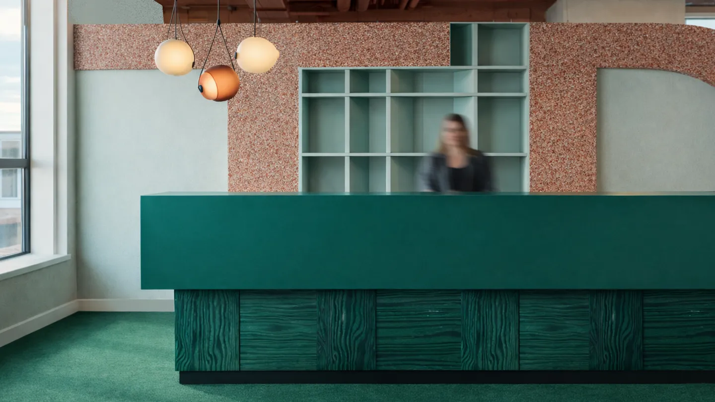 Empfangsbereich mit grünem Tresen, Pendelleuchten und Regalwand.