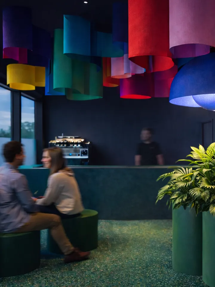 Café-Innenraum mit farbigen Textilstreifen, Sitzmöbeln und Tresenbereich.